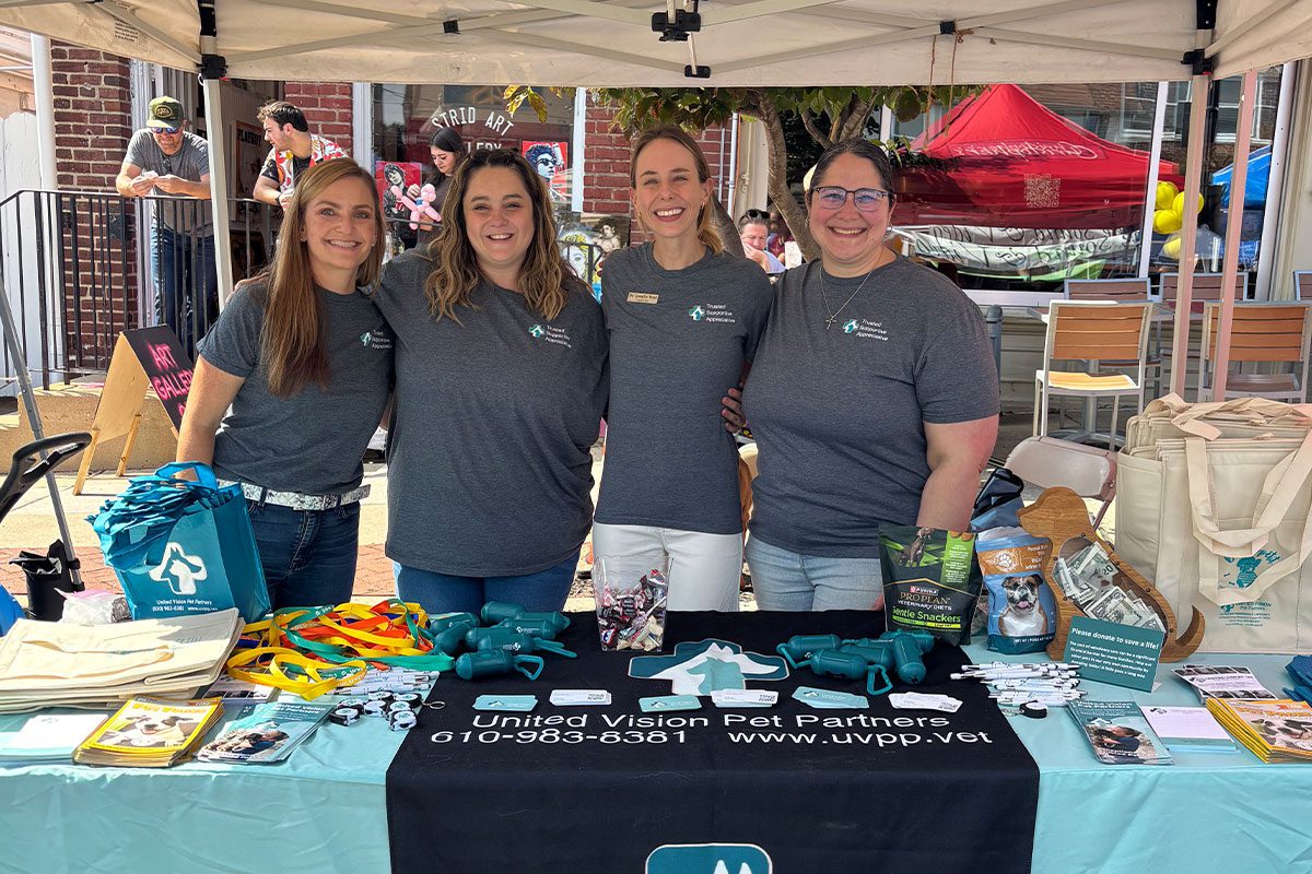4 female staff members smiling and posing behind table booth at Radnor Fall Festival 2025