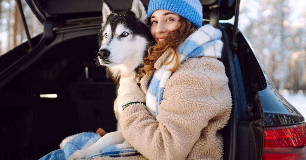 young woman sitting in the back of her car with her husky