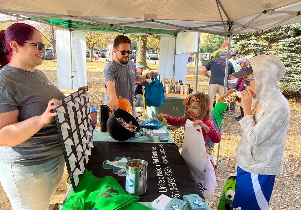 two staff members talking to children at table booth at Bark at the Park Fundraiser 2024
