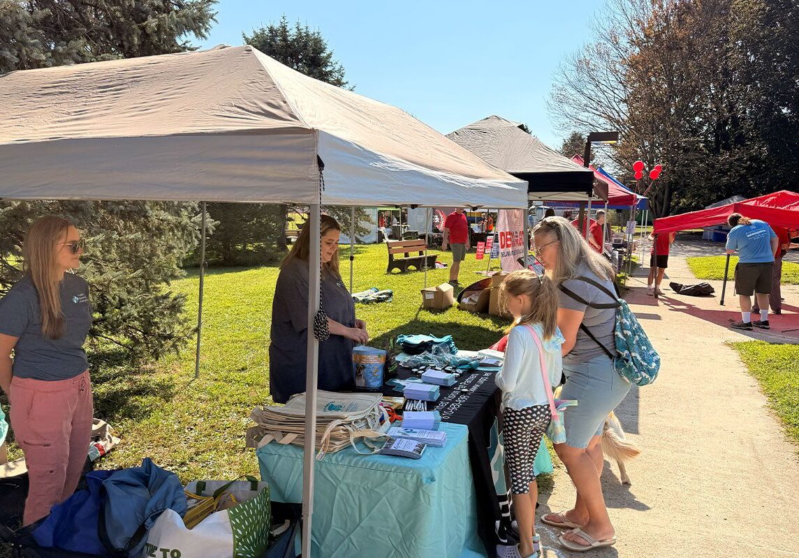 two staff members talking to children and parent at table booth at Upper Providence Township Community Day 2025